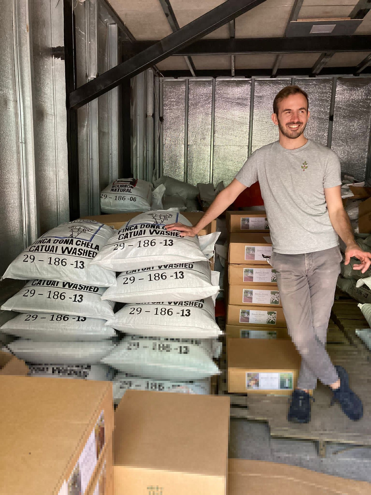 Bastian Harth beside stacked sacks of parchment coffee in a warehouse